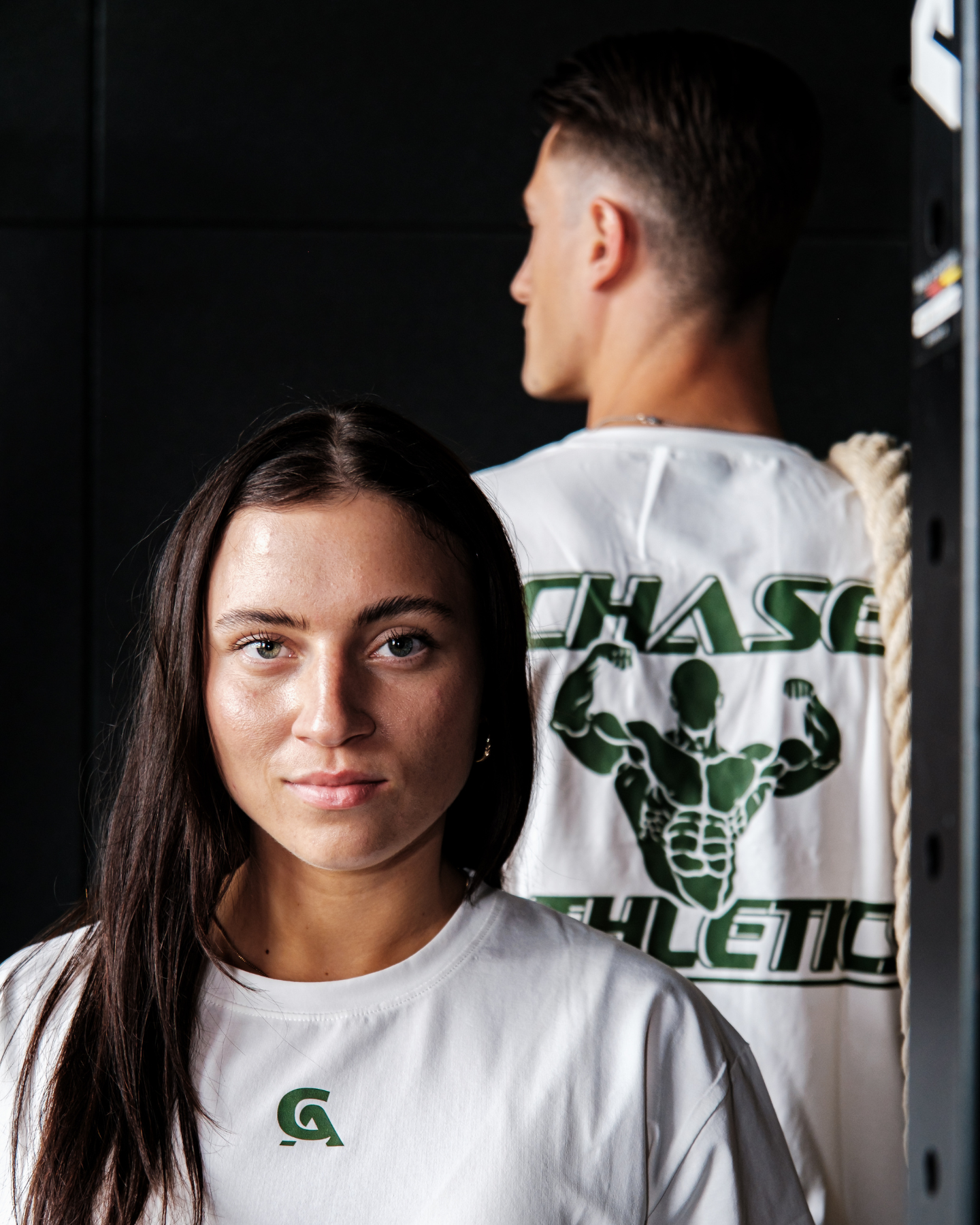 Twee modellen dragen het CHASE ATH Oversized Lifting T-Shirt, unisex fit met streetwear geïnspireerde groene backprint.